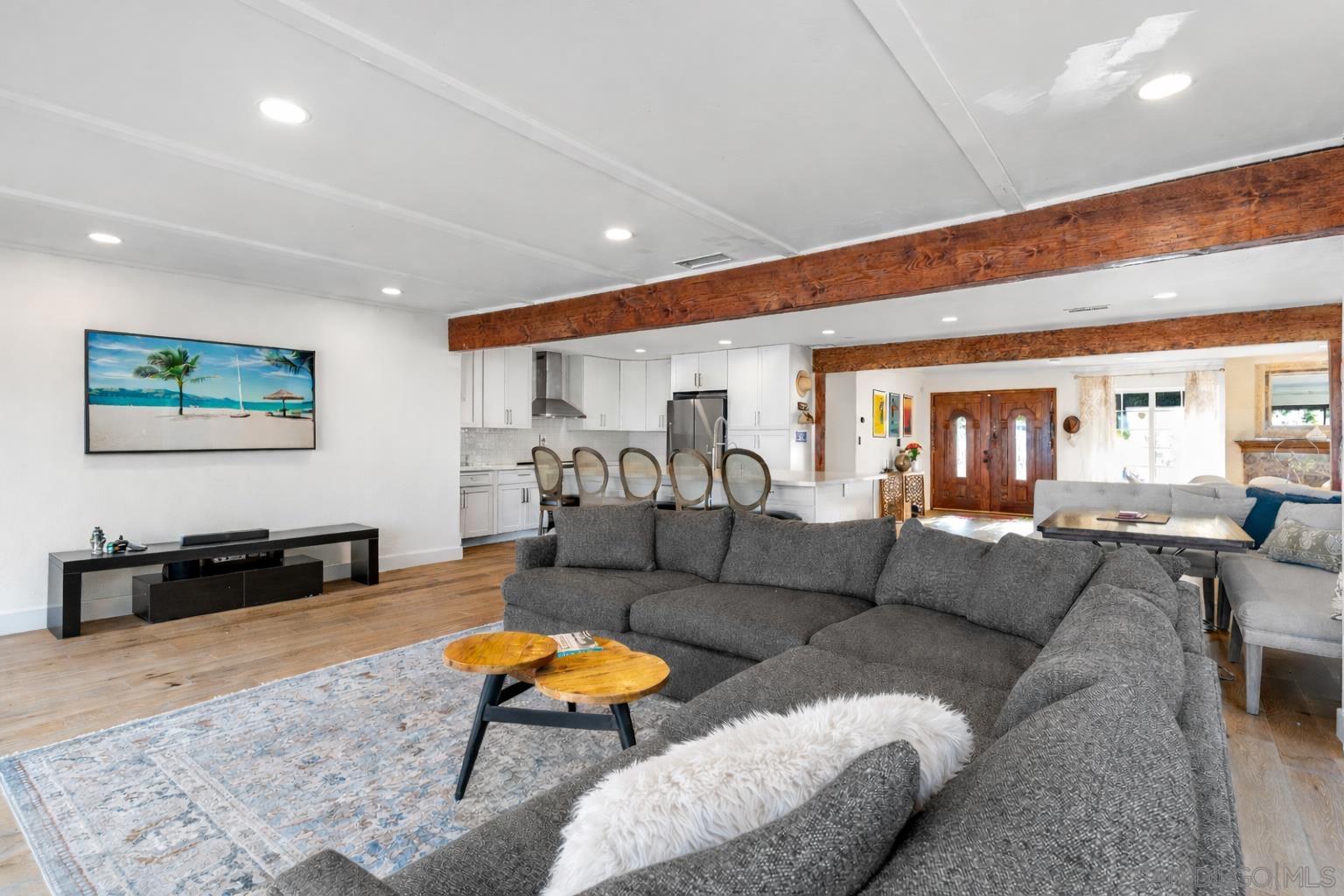 Great room open-plan flow with exposed wood beams, kitchen and dining beyond